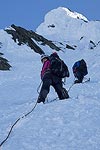 Because of the steepness and the hard snow/ice, we ended up setting anchors with pickets most of the way up.  Brooke is checking out the view as Steve sets an anchor.